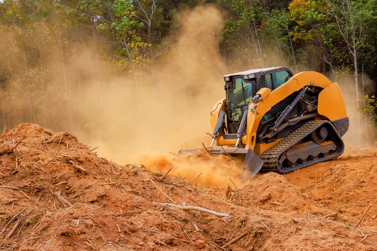 Skid steer clearing a plot of land, moving soil and brush