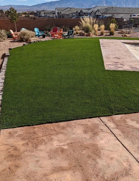 Backyard with artificial green lawn, patio, and colorful Adirondack chairs against mountain backdrop